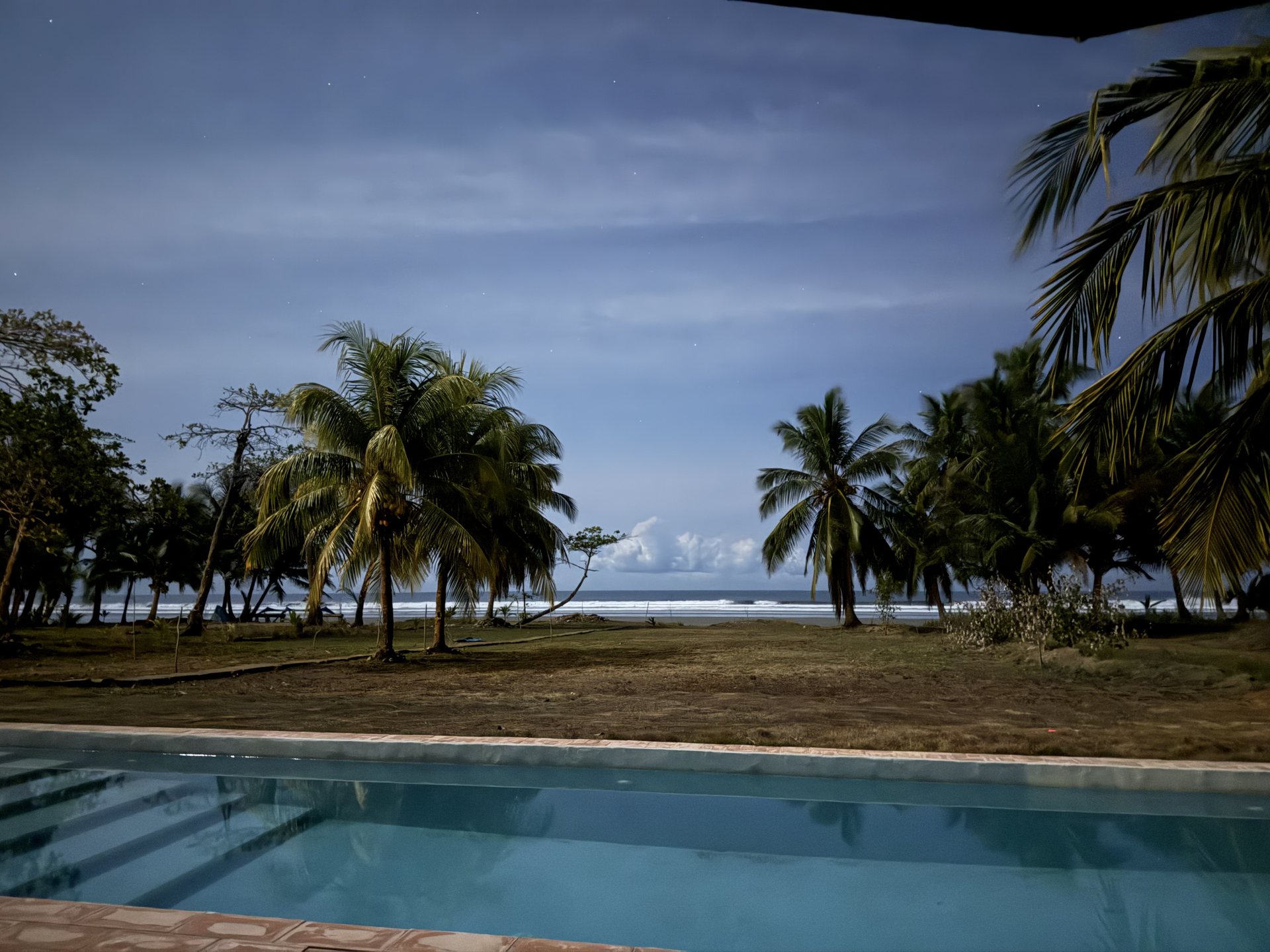View from the pool deck through palms to the ocean at dusk, Mar del Sol Costa Rica