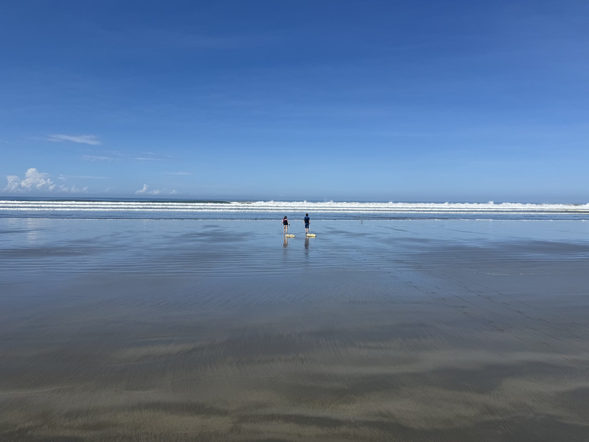 Children playing on the empty wet sand of Playa Coyote at low tide, family beach Costa Rica